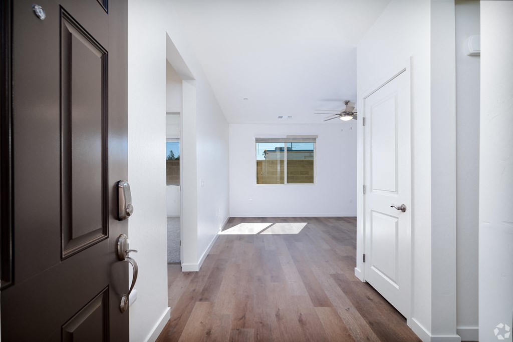 a hallway with white walls and wood floors and a brown entry door